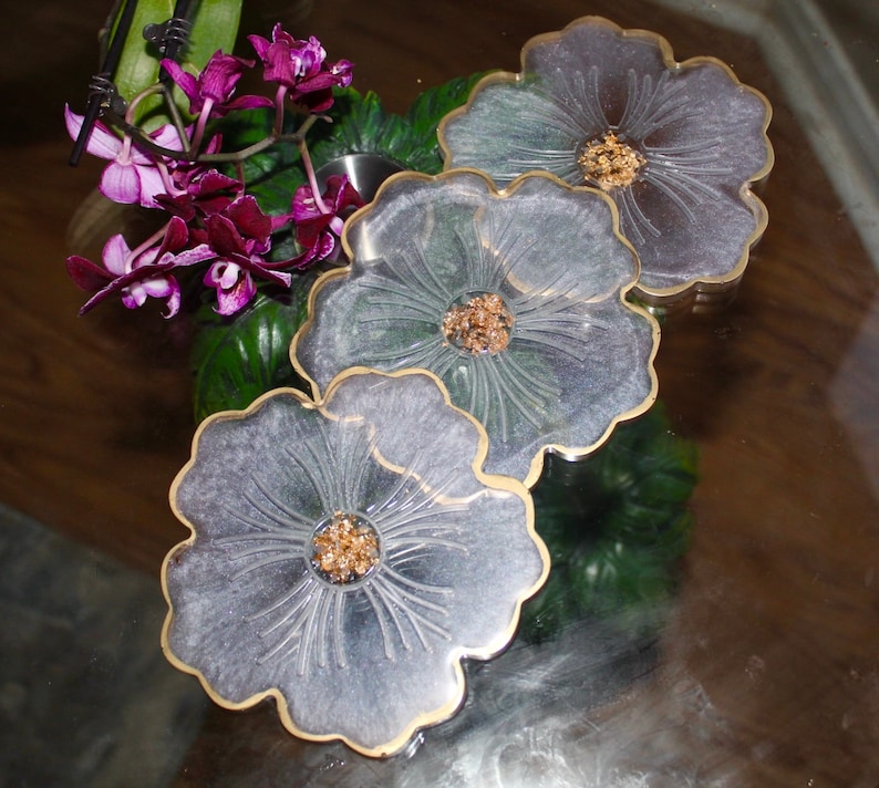 May include: Three gray resin coasters with a gold rim and a floral design. Each coaster features a raised flower with a gold glitter center.