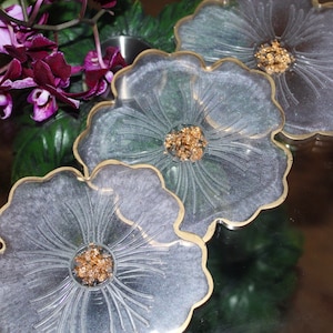 May include: Three clear resin flower-shaped coasters with gold trim and gold glitter accents.