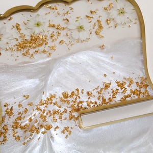 May include: Decorative resin trays with a scalloped edge and gold trim. The trays are white with gold leaf accents and small white flowers embedded in the resin. The design has a pearlescent, shimmering effect.
