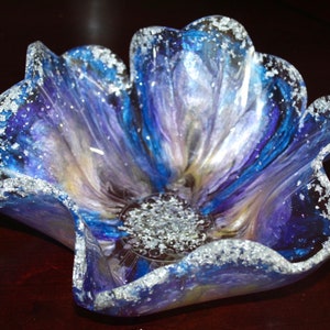 May include: A blue and purple flower-shaped glass bowl with silver glitter accents. The bowl is made of resin and has a unique, handmade look.