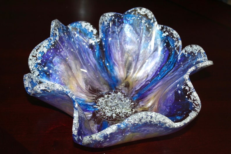 May include: A blue and purple flower-shaped glass bowl with silver glitter accents. The bowl is made of resin and has a unique, handmade look.