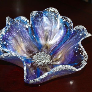 May include: A blue, purple and silver resin flower-shaped bowl with a wavy edge. The bowl has a sparkly finish.