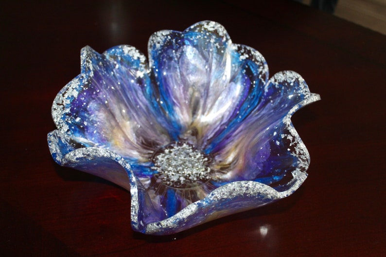 May include: A blue, purple and silver resin flower-shaped bowl with a wavy edge. The bowl has a sparkly finish.