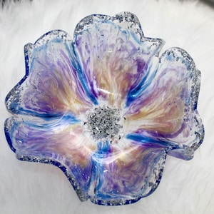 May include: A clear glass flower-shaped bowl with a blue, purple, and white marbled design. The bowl has a silver glitter rim and a silver glitter centre.