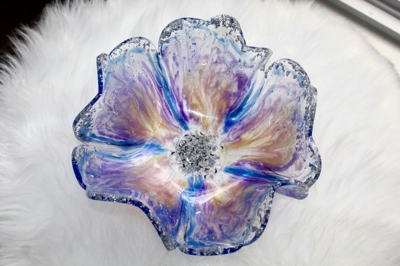 May include: A clear glass flower-shaped bowl with a blue, purple, and white marbled design. The bowl has a silver glitter rim and a silver glitter centre.