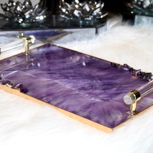 May include: A rectangular serving tray with a purple and white marbled design and gold trim. The tray has two clear acrylic handles with gold accents and is decorated with amethyst crystals.
