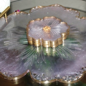 May include: A large, flower-shaped serving tray made of clear resin with a gold rim. The tray has a smaller, flower-shaped coaster in the center, also with a gold rim.