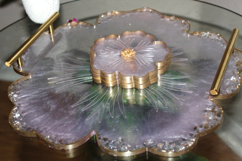 May include: A large, flower-shaped serving tray made of clear resin with a gold rim. The tray has a smaller, flower-shaped coaster in the center, also with a gold rim.