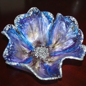 May include: A blue, purple and silver resin flower bowl with a wavy edge. The bowl is made to look like a flower with a centre of silver glitter.