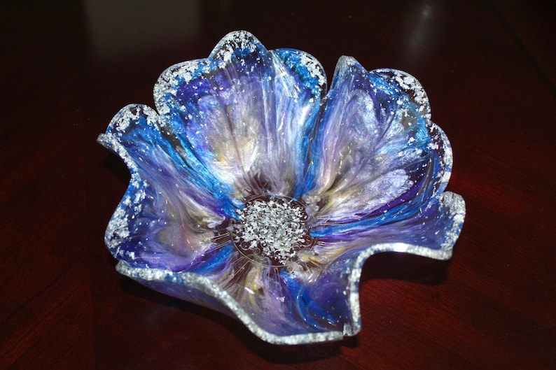 May include: A blue, purple and silver resin flower bowl with a wavy edge. The bowl is made to look like a flower with a centre of silver glitter.