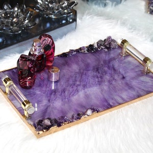 May include: A purple tray with gold trim and clear handles. The tray is filled with amethyst crystals and has three glass bottles of perfume on top.