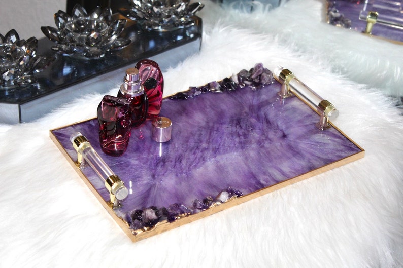 May include: A purple tray with gold trim and clear handles. The tray is filled with amethyst crystals and has three glass bottles of perfume on top.