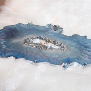 May include: A decorative resin tray with a blue and white marbled design. The tray has a unique, organic shape and is embellished with small, sparkling crystals. The tray is approximately 10 inches long and 7 inches wide.