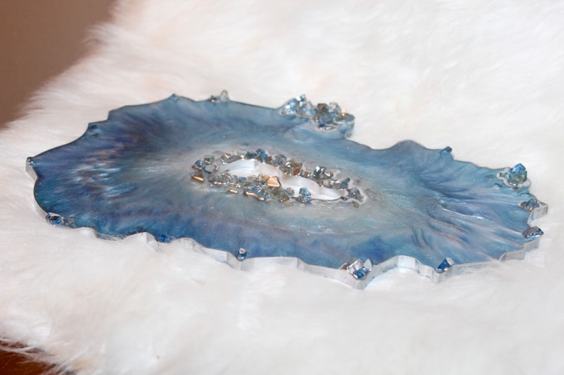 May include: A decorative resin tray with a blue and white marbled design. The tray has a unique, organic shape and is embellished with small, sparkling crystals. The tray is approximately 10 inches long and 7 inches wide.