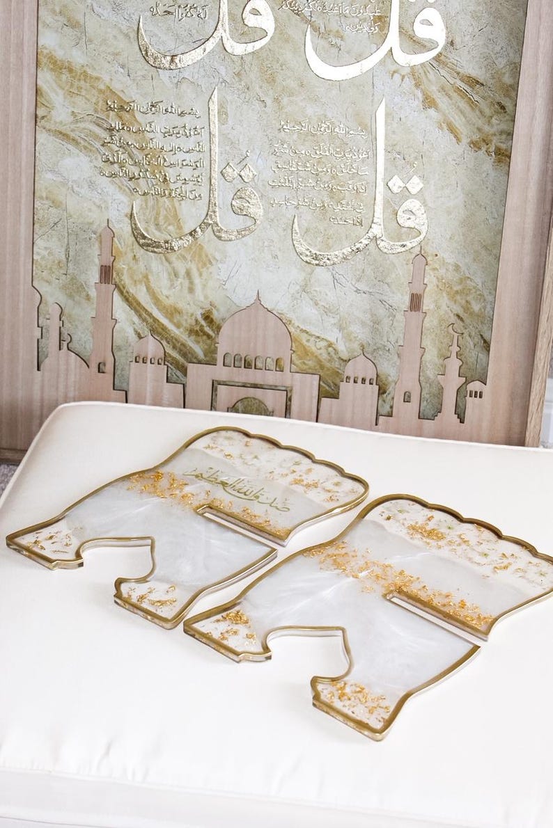May include: Decorative Islamic art piece featuring a wooden mosque silhouette and a framed artwork with Arabic calligraphy in gold. Four clear, resin-like coasters with gold accents are in the foreground.