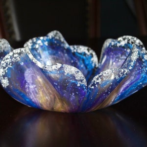 May include: A blue and purple glass bowl with a wavy edge and silver glitter accents. The bowl is shaped like a flower.