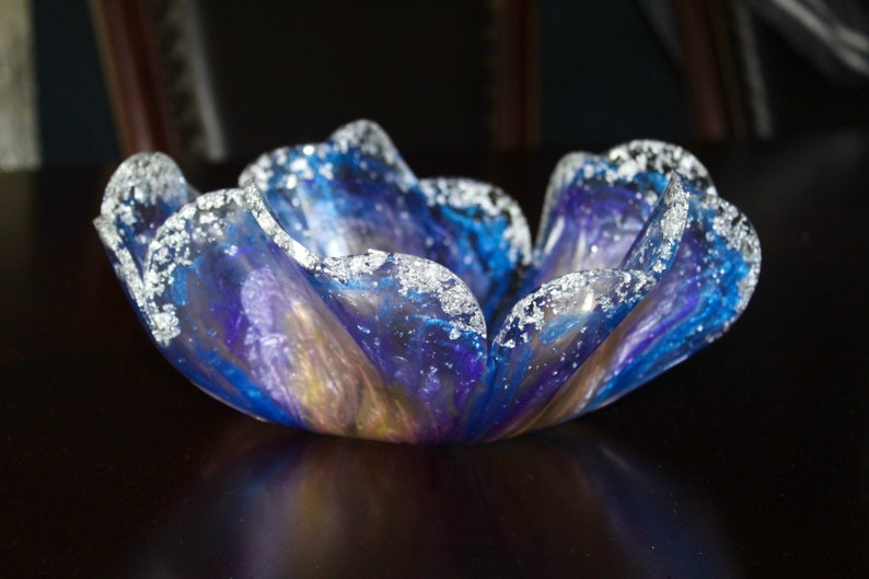 May include: A blue and purple glass bowl with a wavy edge and silver glitter accents. The bowl is shaped like a flower.