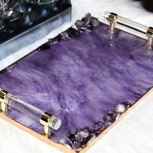May include: A rectangular serving tray with a purple resin base and gold trim. The tray has two clear acrylic handles and is decorated with amethyst crystals.