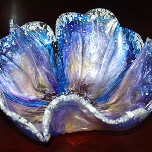 May include: A blue, purple and white resin bowl with a flower-like shape and a silver glitter rim.