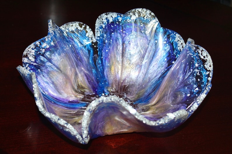 May include: A blue, purple and white resin bowl with a flower-like shape and a silver glitter rim.
