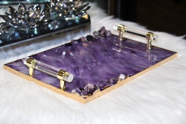 May include: A rectangular serving tray with a purple resin base and gold trim. The tray has two clear acrylic handles and is decorated with small amethyst crystals.