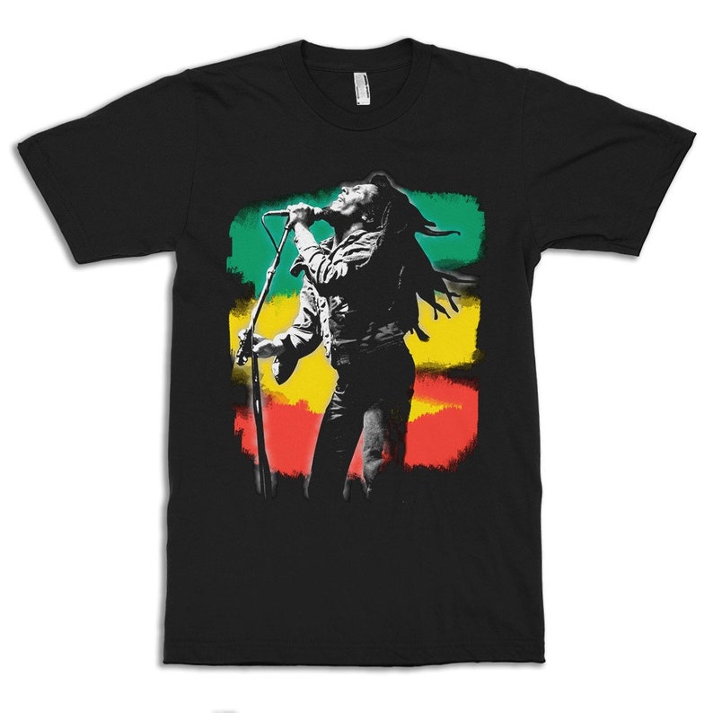 May include: Black t-shirt with a graphic of Bob Marley singing into a microphone in front of a red, yellow, and green background.