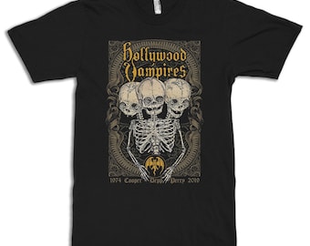 May include: Black t-shirt featuring a graphic of three skeletal heads with a single skeleton body. The graphic is surrounded by an ornate frame with the text "Hollywood Vampires" in gold lettering. The text "1974 Cooper Depp Perry 2019" is below the graphic.