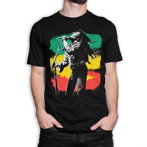 May include: Black t-shirt with a silhouette of Bob Marley singing into a microphone in front of a colorful background of green, yellow, and red.