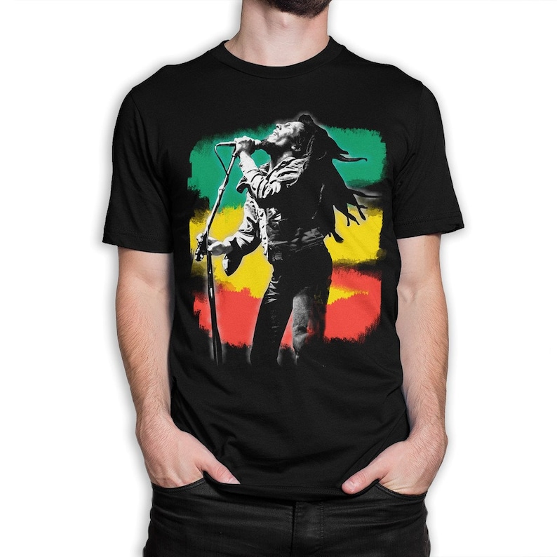 May include: Black t-shirt with a silhouette of Bob Marley singing into a microphone in front of a colorful background of green, yellow, and red.