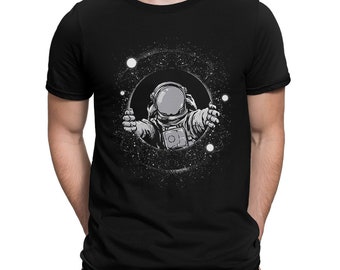 May include: A black t-shirt with a graphic of an astronaut floating in space. The astronaut is wearing a white spacesuit and has a black helmet. The background is a black and white galaxy with stars.