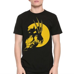 May include: A black short-sleeved t-shirt featuring a yellow graphic print of the character Wolverine. The design shows the character in a dynamic pose with extended claws against a large yellow circular background, centred on the chest.