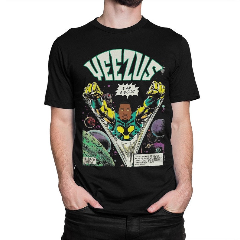 May include: Black t-shirt with a comic book style graphic of a man in a green and yellow suit with the word "YEEZUS" in large letters above him. The text "I AM A GOD!" is in a speech bubble above the man's head. The comic book panel is set in space with planets and stars in the background.