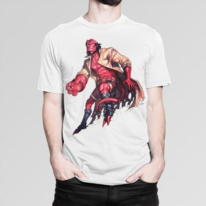 May include: White t-shirt with a graphic print of a red, horned, superhero character with a large right hand, wearing a brown trench coat and black pants. The character is standing with his right leg raised and his left hand on his hip.