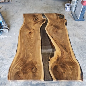 Op de afbeelding: Een groot houten tafelblad met een levende rand en een zwarte epoxyrivier die door het midden loopt.
