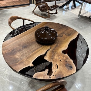 May include: A round wooden table with a black epoxy resin inlay. The table has a natural wood grain and a dark brown finish. A brown ceramic vase sits on the table.