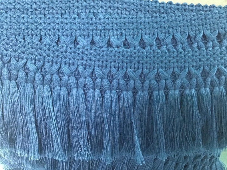 May include: Blue tassel trim with a woven design. The trim has a fringe of tassels that are about 1 inch long.