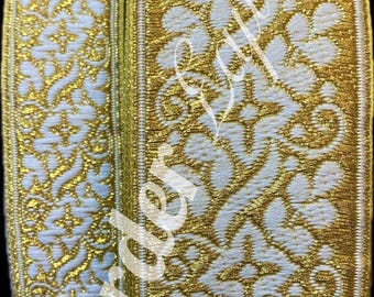 Op de afbeelding: Close-up van twee rollen decoratieve sierband. De sierband heeft een witte achtergrond met een sierlijk gouden bloemmotief. De randen zijn ook goudkleurig afgewerkt. De sierband wordt waarschijnlijk gebruikt voor naaien, knutselen of verfraaien.