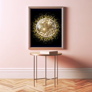 May include: A framed print of a gold disco ball with a black background and gold glitter. The print is hanging on a pink wall above a gold metal table.