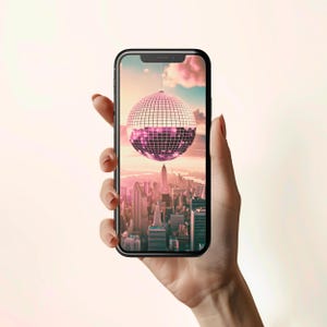 Może przedstawiać: Smartfon wyświetlający panoramę miasta z dyskotekową kulą wiszącą w powietrzu nad budynkami. Niebo jest różowe i pomarańczowe z chmurami.