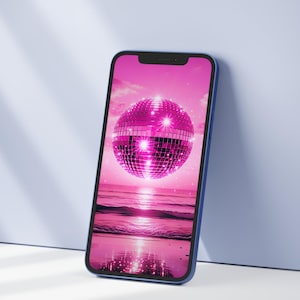 May include: A blue smartphone shows a pink image of a disco ball above a beach scene. The disco ball is the main focus, reflecting light. The phone is propped against a light blue surface.