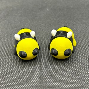 May include: Two small, black and yellow bee figurines with white wings. The bees are facing forward with their wings out.