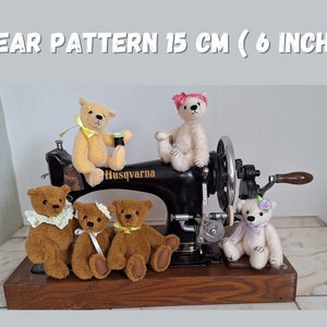May include: Five teddy bears of different colours and designs are arranged on a vintage sewing machine. The bears are all about 15 cm tall. The sewing machine is black with a wooden base. The bears are all wearing different accessories, such as bows, ribbons, and flowers.