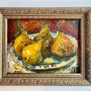 May include: An oil painting of four yellow and green pears resting on a patterned plate, set against a dark red background. The artwork is enclosed in an ornate, metallic gold-toned frame with intricate embossed scrollwork along the edges.