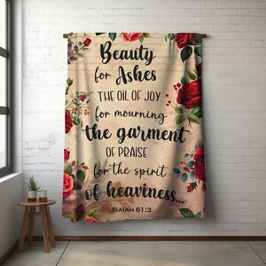Puede incluir: Un tapiz beige con un diseño floral con rosas rojas. El tapiz tiene una cita de Isaías 61:3: "Belleza por ceniza, aceite de alegría por luto, vestidura de alabanza por espíritu de tristeza."