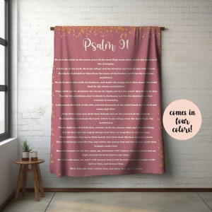 May include: A dusty rose colored blanket featuring the full text of Psalm 91 in white lettering. The top and bottom edges of the blanket are decorated with a gold speckled pattern. A circular pink graphic on the right side reads comes in four colors.