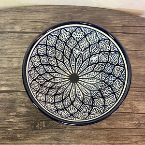 Könnte beinhalten: Eine weiße Keramikschüssel mit einem blauen und weißen geometrischen Muster. Die Schüssel ist rund und hat einen breiten Rand.