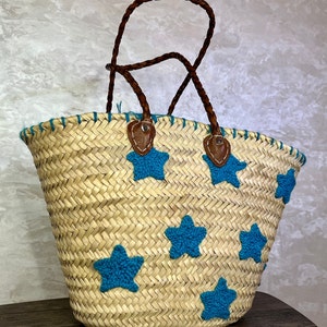 May include: A woven straw tote bag with blue star embroidery and brown leather handles.
