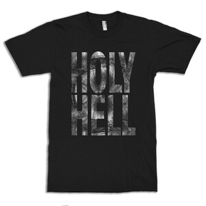 Op de afbeelding: Zwart T-shirt met een witte grafische print van de woorden "HOLY HELL" in een distressed stijl.