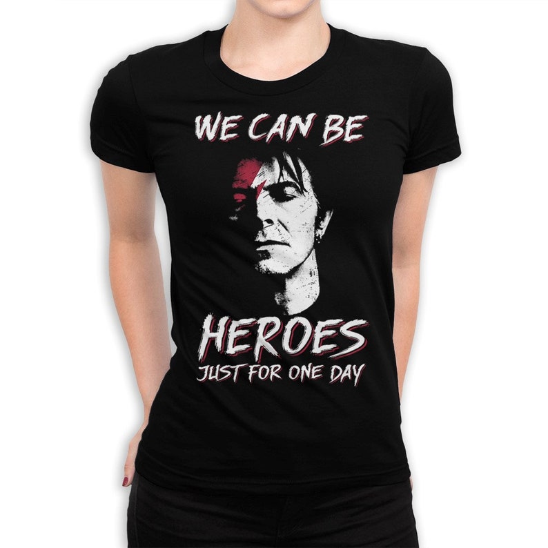May include: Black t-shirt with a white graphic of a man's face with a red stripe across his eye. The text "WE CAN BE HEROES JUST FOR ONE DAY" is printed below the image.