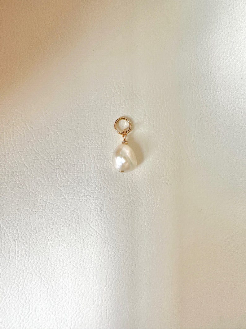 May include: A white baroque pearl charm with a gold jump ring.